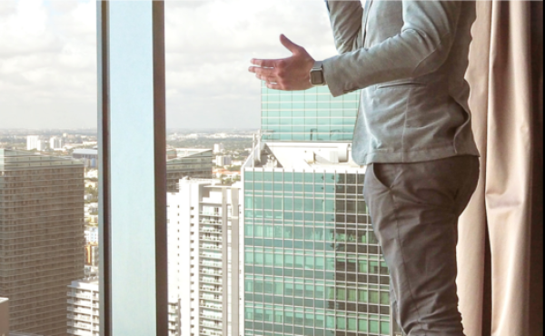the torso of a man on a phonecall in front of a window with a cityscape view