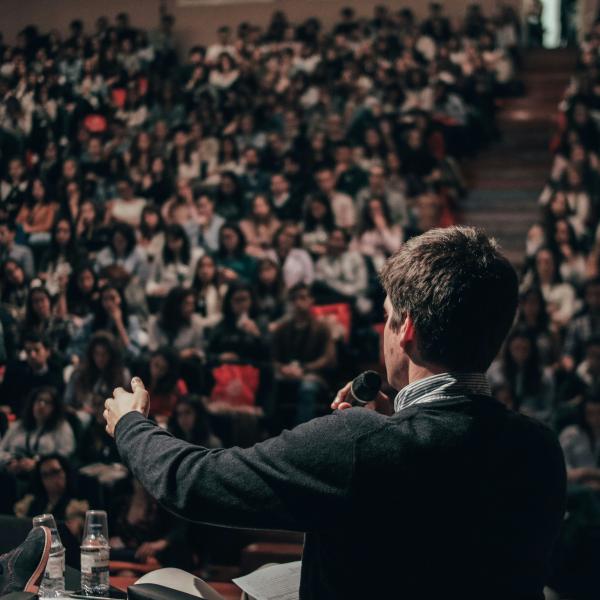 Someone speaking in front of a crowded hall