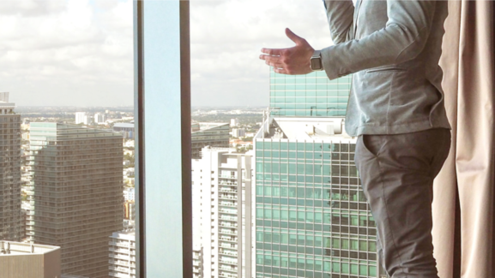 the torso of a man on a phonecall in front of a window with a cityscape view